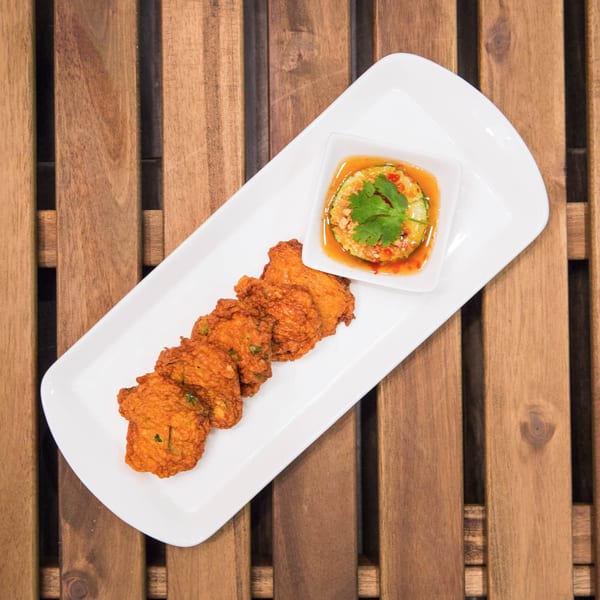 Crispy Thai fish cakes with sweet chili cucumber relish on a white rectangular plate.