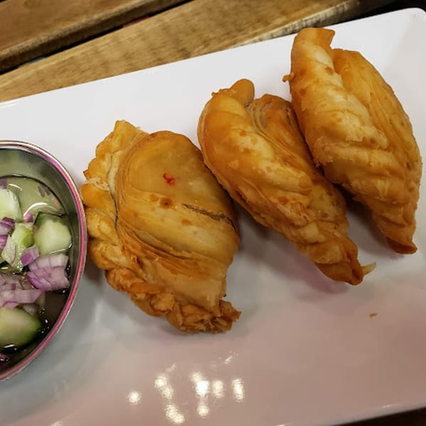Three golden-brown Thai curry puffs with a side of cucumber and red onion relish.