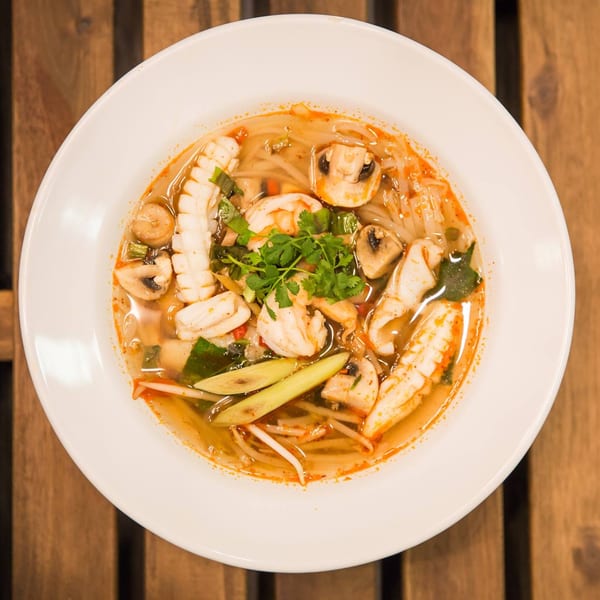 Kao Sarn Thai Street Food's Tom Yum soup with seafood, mushrooms, and herbs in a white bowl.