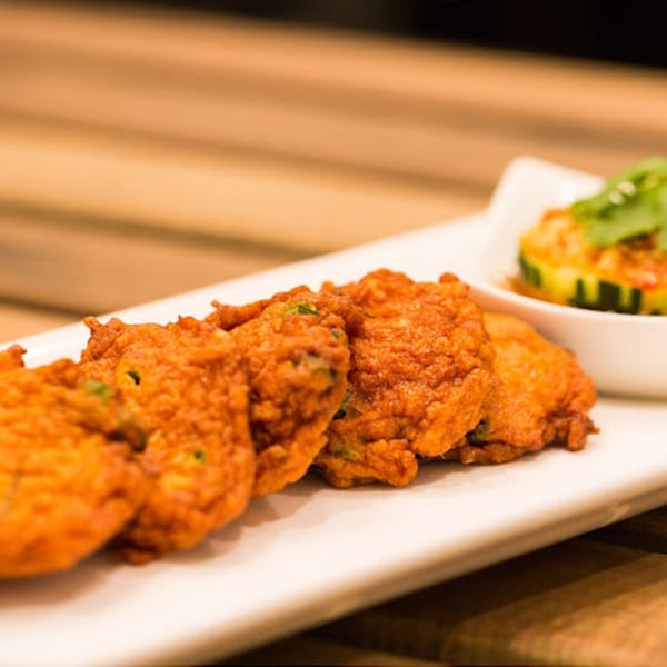 Crispy Thai fish cakes with a side of cucumber relish on a white rectangular plate.